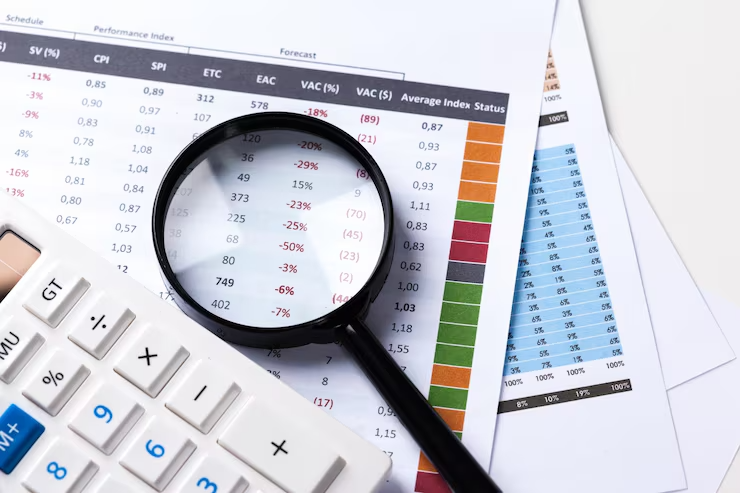 Loupe posée sur un tableau de bord financier chiffré, calculatrice à proximité