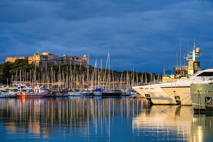 Port de plaisance au crépuscule avec voiliers et yachts amarrés, fort en arrière-plan